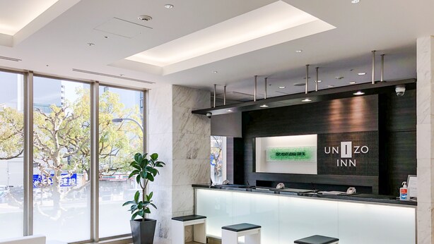 A modern hotel lobby with a reception desk, seating area, and large windows offering a view of the city. - UNIZO INN Hiroshima Ekimae (Hiroshima)