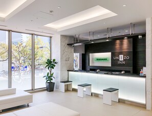 Un hall d’hôtel moderne doté d’un comptoir d’accueil, d’un espace salon et de grandes fenêtres offrant une vue sur la ville.