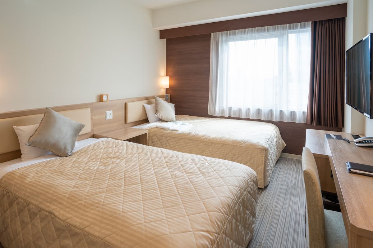 Ein Hotelzimmer mit zwei Betten, einem Schreibtisch, einem Fernseher und einem fenster mit Vorhängen.