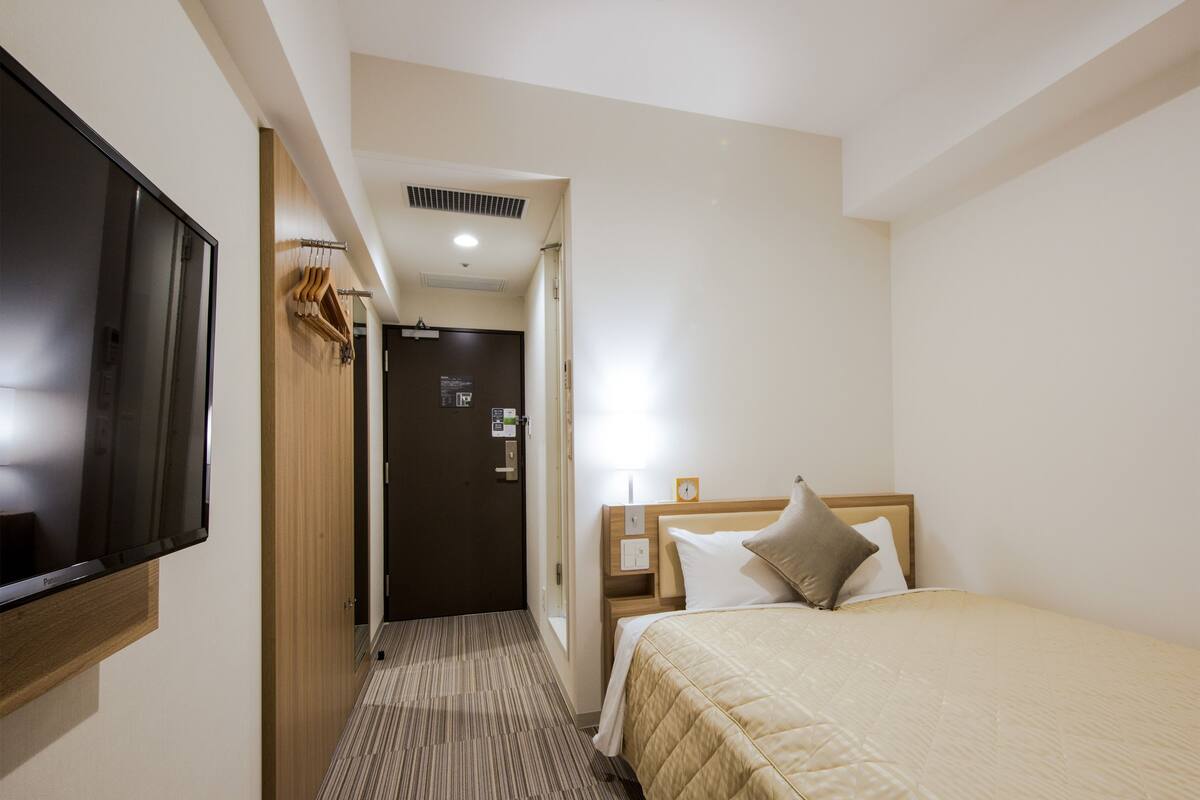 Ein Hotelzimmer mit Bett, Wandfernseher, einer Tür mit Schild und Teppichboden.