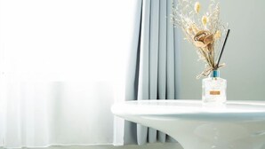 Una mesa blanca con un jarrón de cristal transparente que contiene flores secas y una vela.
