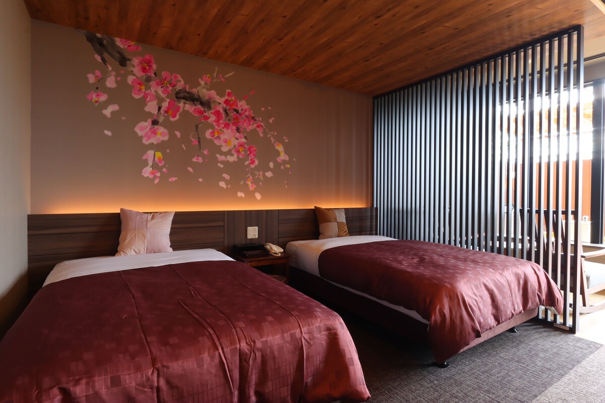 Une chambre d’hôtel avec deux lits, un plafond en bois, un mur orné d’une fresque florale et une porte coulissante.