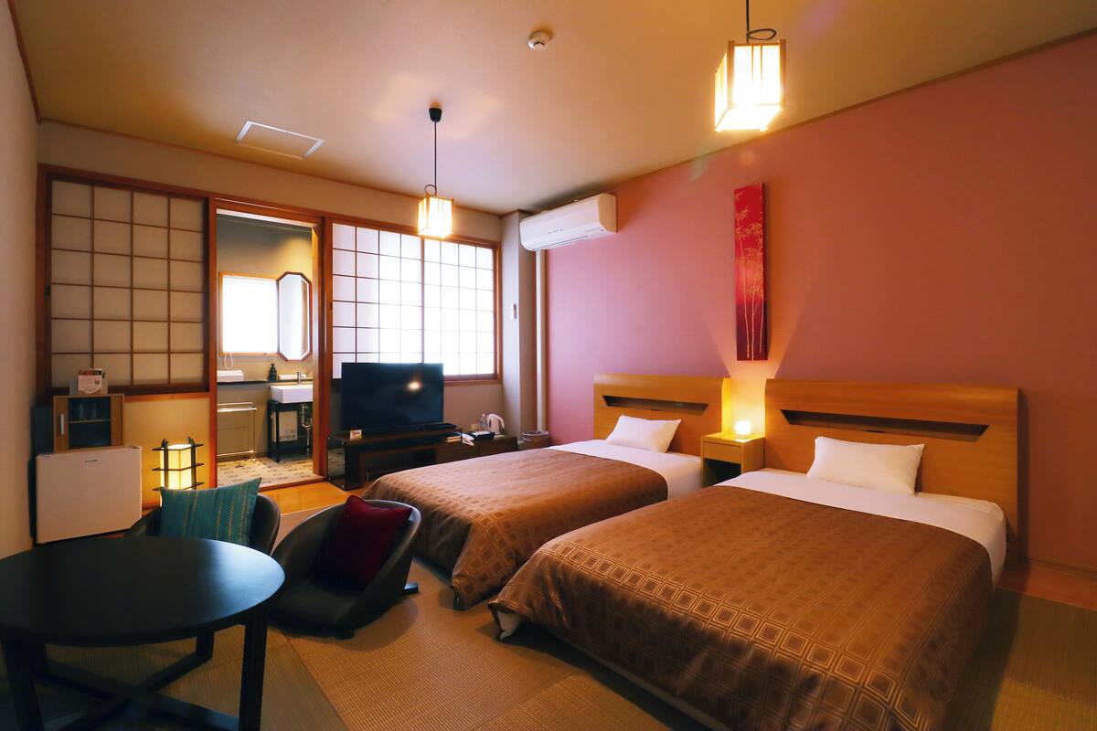Ein Hotelzimmer mit zwei Betten, einem Esstisch, einem Fernseher und einer Küchenzeile.