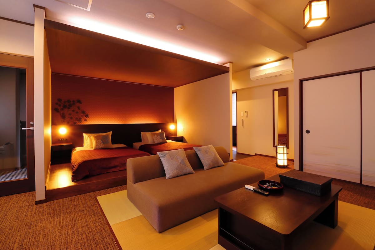 Ein modernes Hotelzimmer mit einer Couch, einem kleinen Tisch, einem Bett mit Kopfteil und einer Schiebetür zu einem Badezimmer.