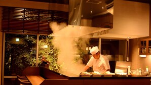 A chef preparing food in a modern kitchen with a view of greenery outside. - Kafutei (Yamaga)