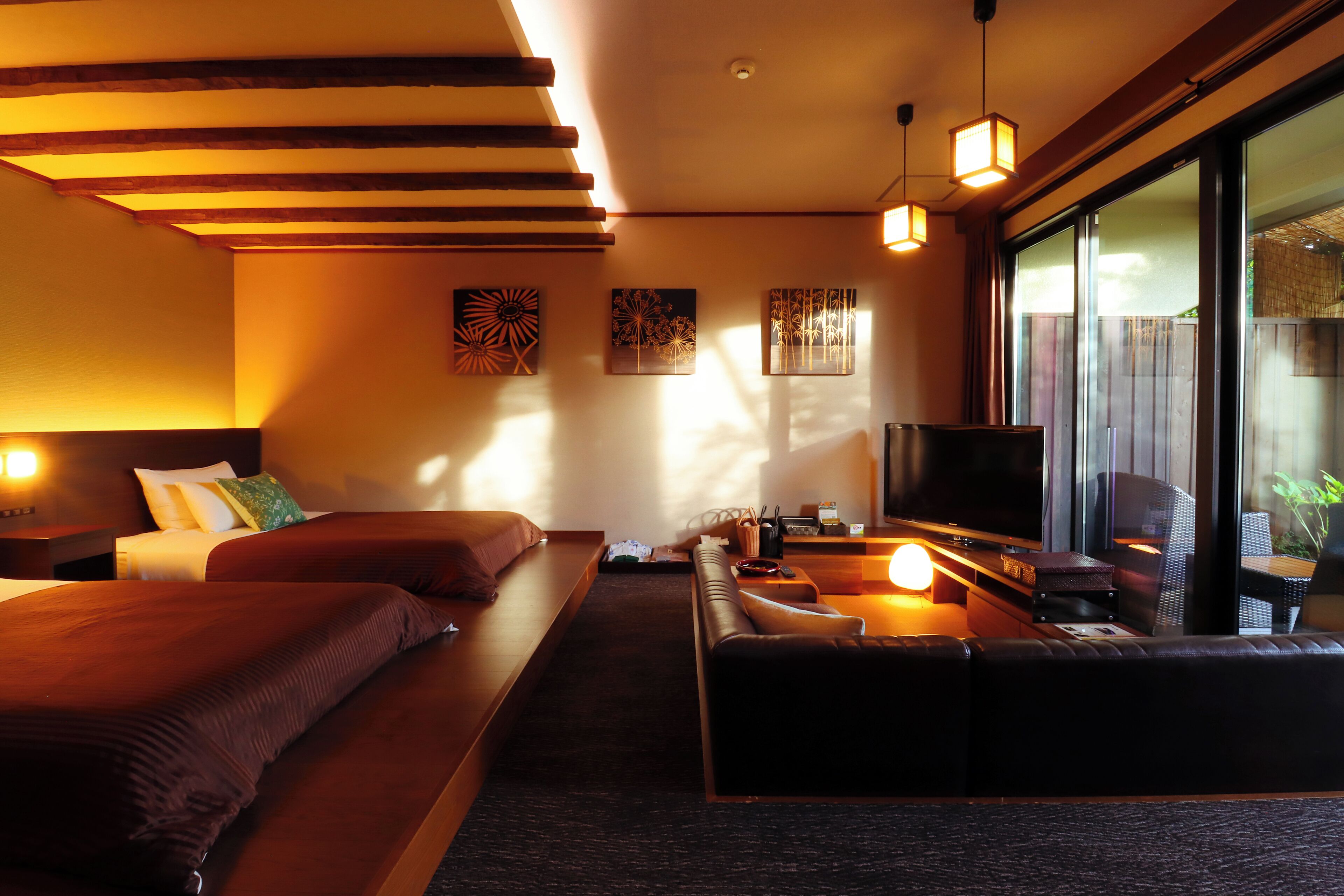 A modern hotel room with a large bed, a sofa, a TV, and a large window.