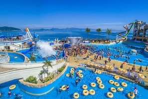 Uma ampla área de piscina ao ar livre com várias escorregas e um palco para eventos.