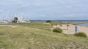 A grassy area with a beach, a blue sign, and a row of white boats in the background.