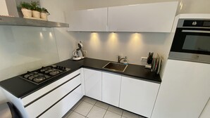 A modern kitchen with white cabinets, a black countertop, a gas stove, a built-in oven, and a stainless steel range hood.