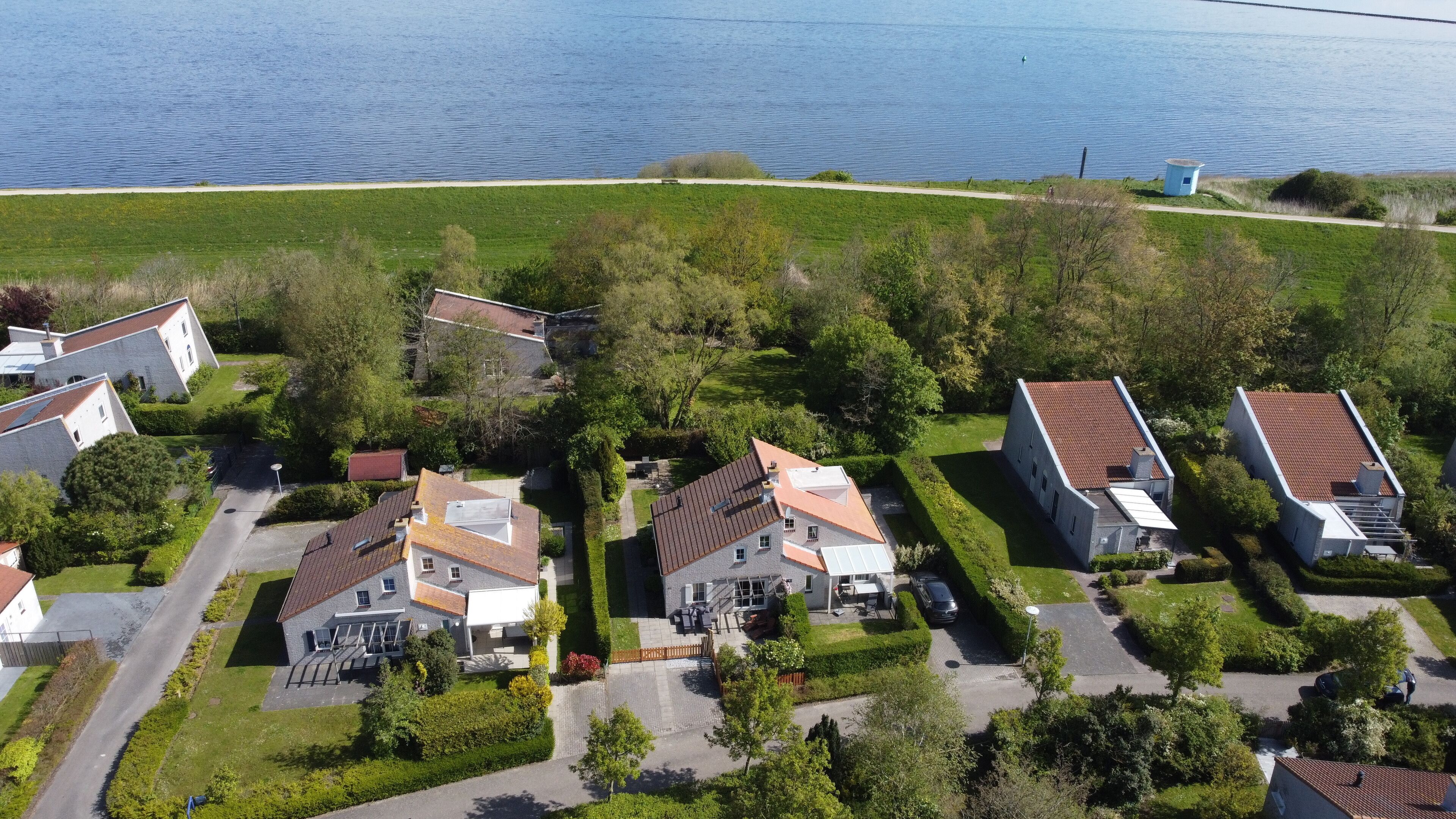 An aerial view of a residential area with houses, a road, and a body of water in the background.