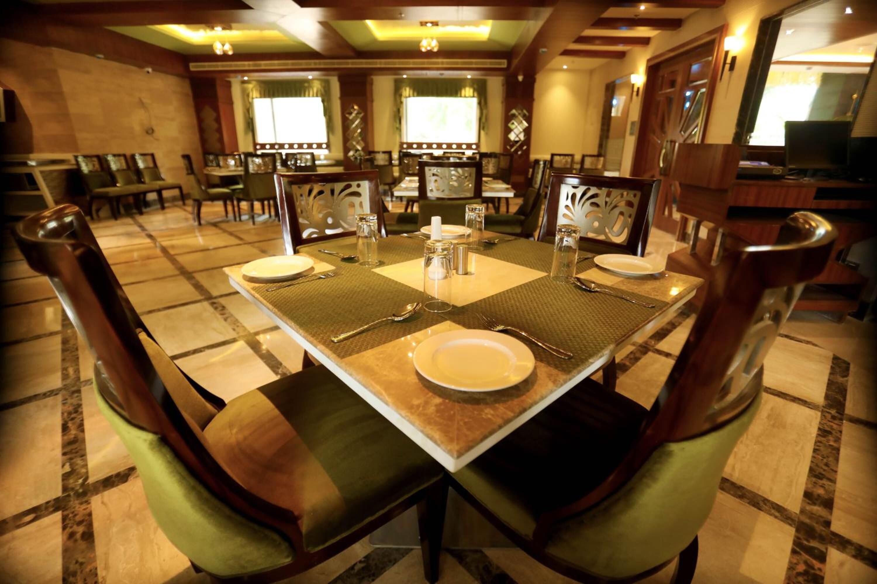 A dining area with a large rectangular table set for four, surrounded by chairs with green upholstery.