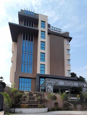 A modern hotel with a central tower, large windows, and a decorative entrance. - The Pinnacle INN Sarnath  (Varanasi)