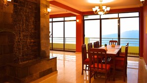 A dining area with a stone fireplace, large windows with a view, and a chandelier. - Hotel Nagarkot Inn (Baluwapati Deupur)