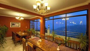 A dining area with a large table and chairs, large windows with a view of the sea, and a chandelier. - Hotel Nagarkot Inn (Baluwapati Deupur)