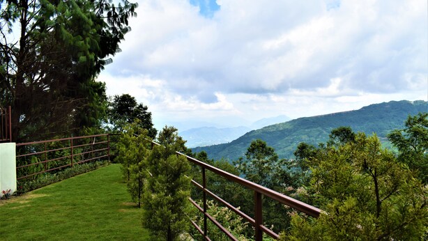 A grassy area with a metal railing overlooking a mountainous landscape. - Hotel Nagarkot Inn (Baluwapati Deupur)