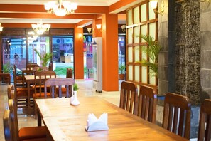 A restaurant with wooden tables and chairs, a stone wall with a water feature, and a view of the street outside. - Hotel Nagarkot Inn (Baluwapati Deupur)