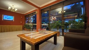 A lobby with a wooden table, potted plants, a television, and large windows. - Hotel Nagarkot Inn (Baluwapati Deupur)