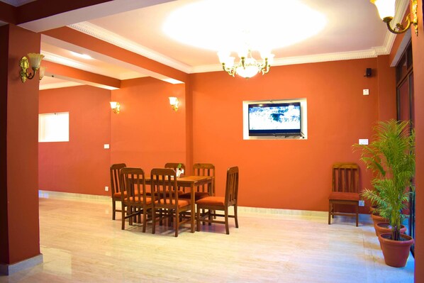 A dining area with a table and chairs, a television mounted on the wall, and a chandelier. - Hotel Nagarkot Inn (Baluwapati Deupur)