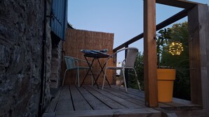 Terraza de madera con una mesa y dos sillas, un muro azul y una cerca de madera.