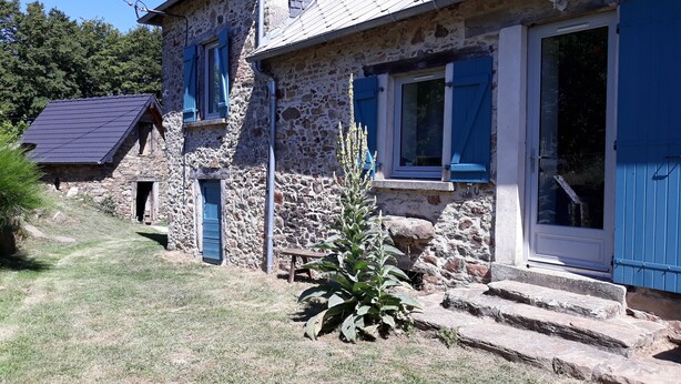 Una casa de piedra con contraventanas azules y un pequeño jardín.
