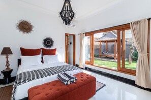 A modern bedroom with a large bed, a red ottoman, and a view of a garden through large sliding doors. - Villa Four Elements (Canggu)