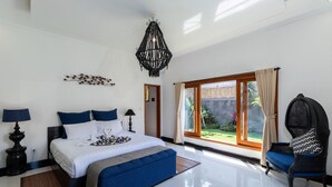 A modern bedroom with a large bed, a blue sofa, a decorative chandelier, and a view of the outdoors. - Villa Four Elements (Canggu)