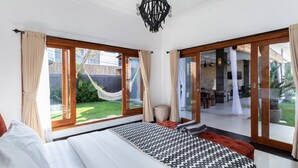 A bedroom with a large bed, a view of the garden, and a sliding glass door leading to a patio area. - Villa Four Elements (Canggu)