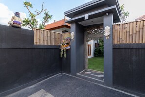 A modern entrance with a dark facade, a wooden fence, and a decorative wall piece. - Villa Four Elements (Canggu)