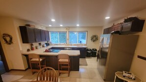 A kitchen with a central island, two bar stools, a refrigerator, and a dining table with chairs. - Moondance lodge is a place you can go and relax and access the outdoors (Index)