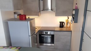 A compact kitchen with a built-in oven, a refrigerator, and a small dining table. - Vacation cottage *** - Panoramic view - Sauna - Near lake - Mountain (Saulxures-sur-Moselotte)