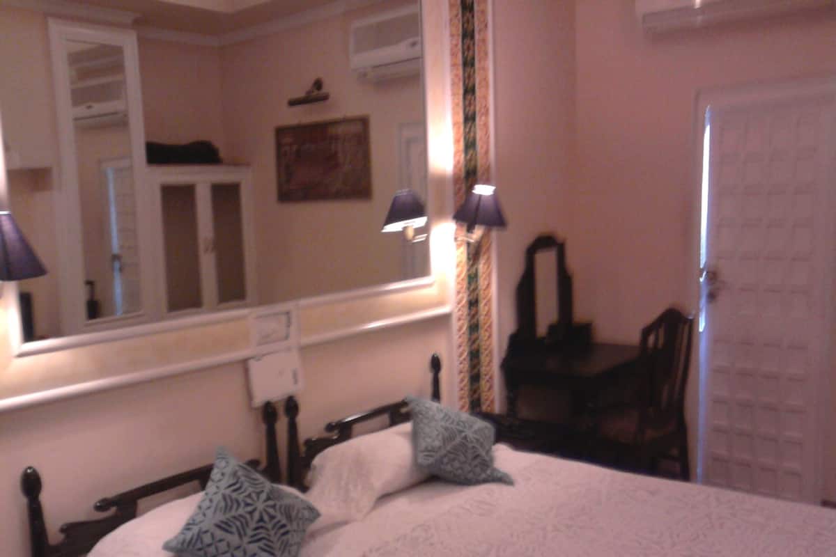 Ein Schlafzimmer mit einem Bett, zwei Kissen, einem Spiegel, einem Schminktisch und einem Sessel.
