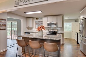 A modern kitchen with a central island, bar stools, stainless steel appliances, and a view to the outside. - Modern Home w/ Yard + Deck, 1 Mi to Clemson U! (Clemson)