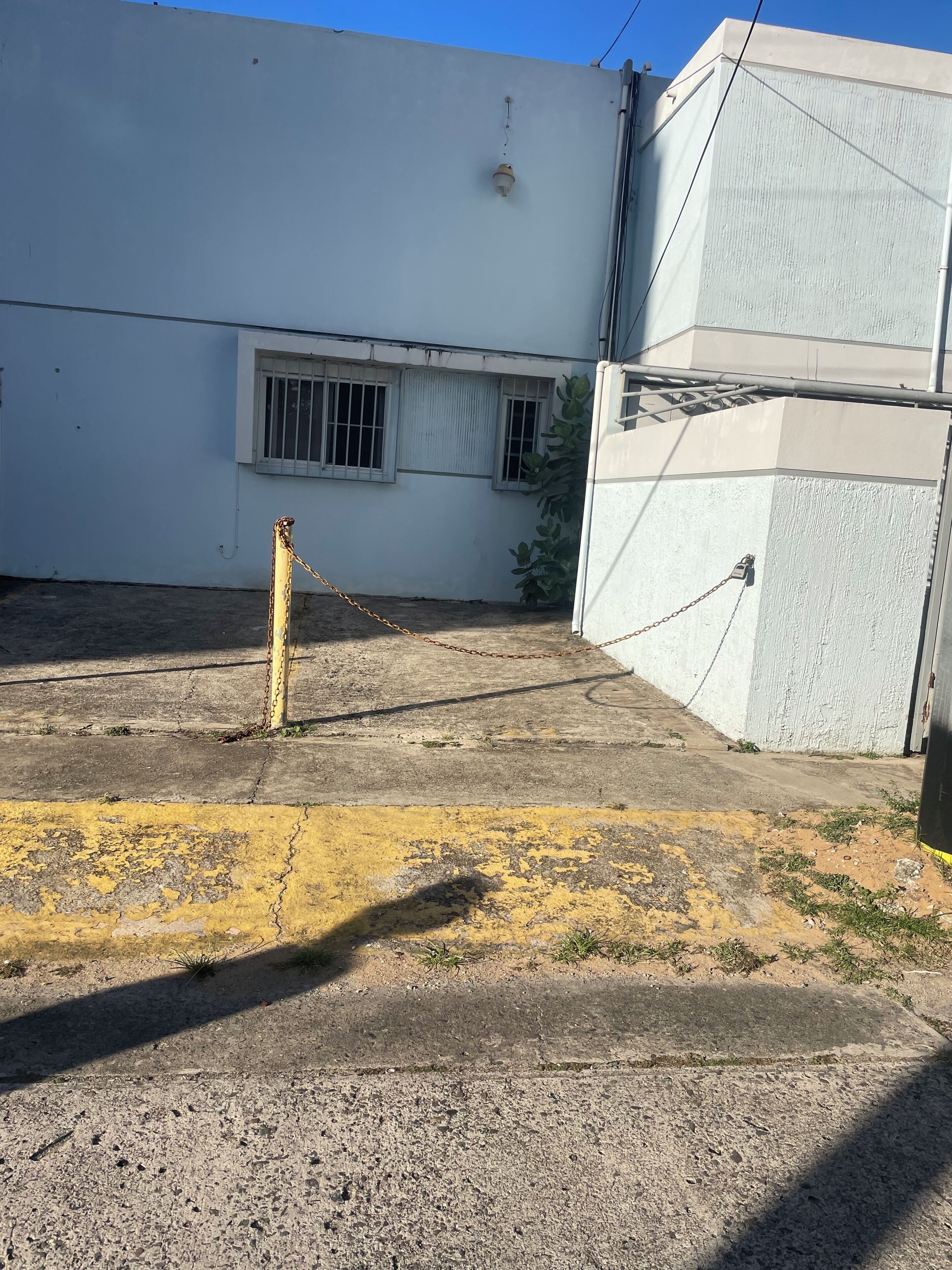 Un bâtiment doté d’un portail fermé par une chaîne, d’un sol en béton et d’une fenêtre grillagée.