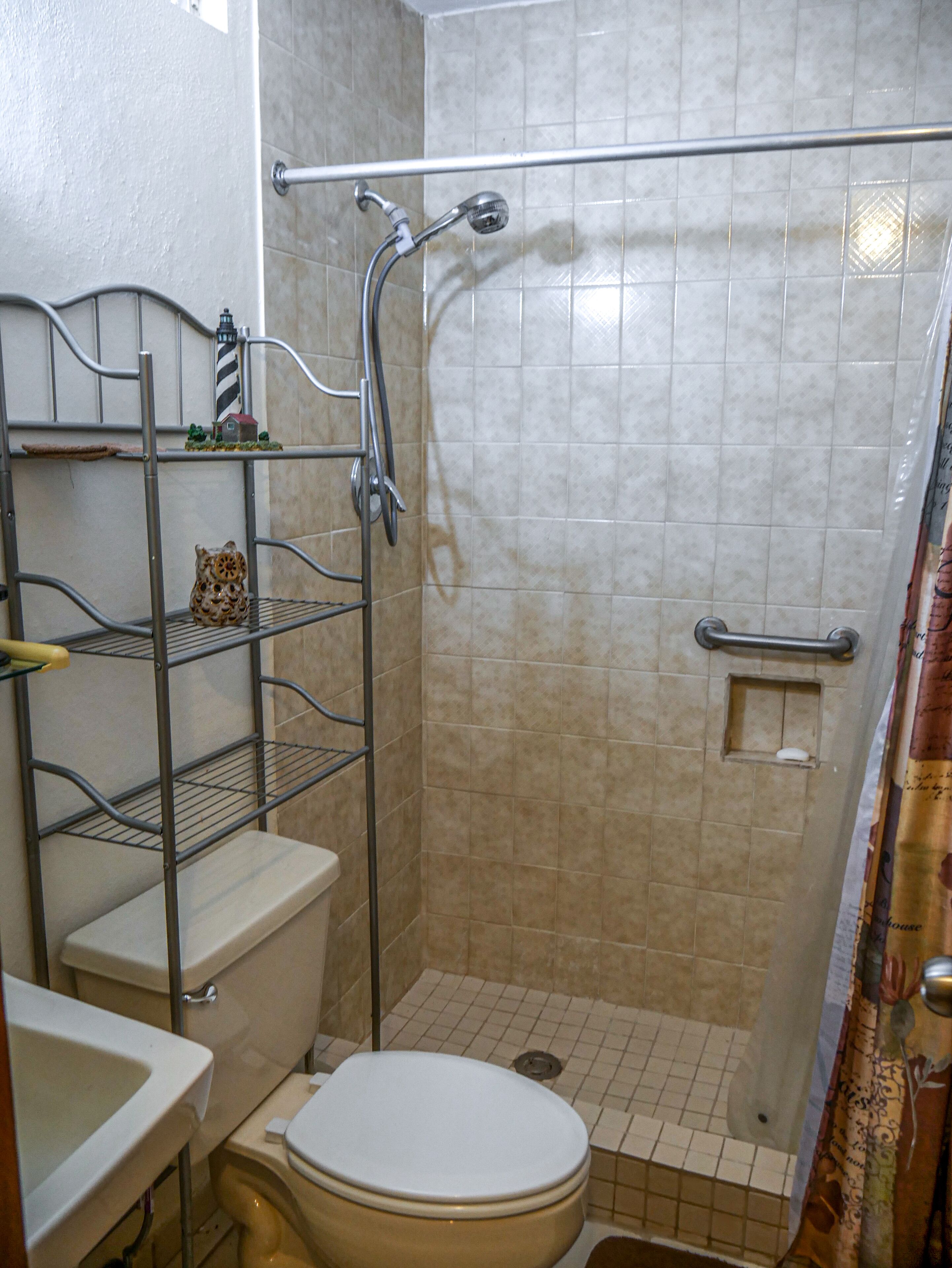 A bathroom with a shower, toilet, and a metal shelf unit.