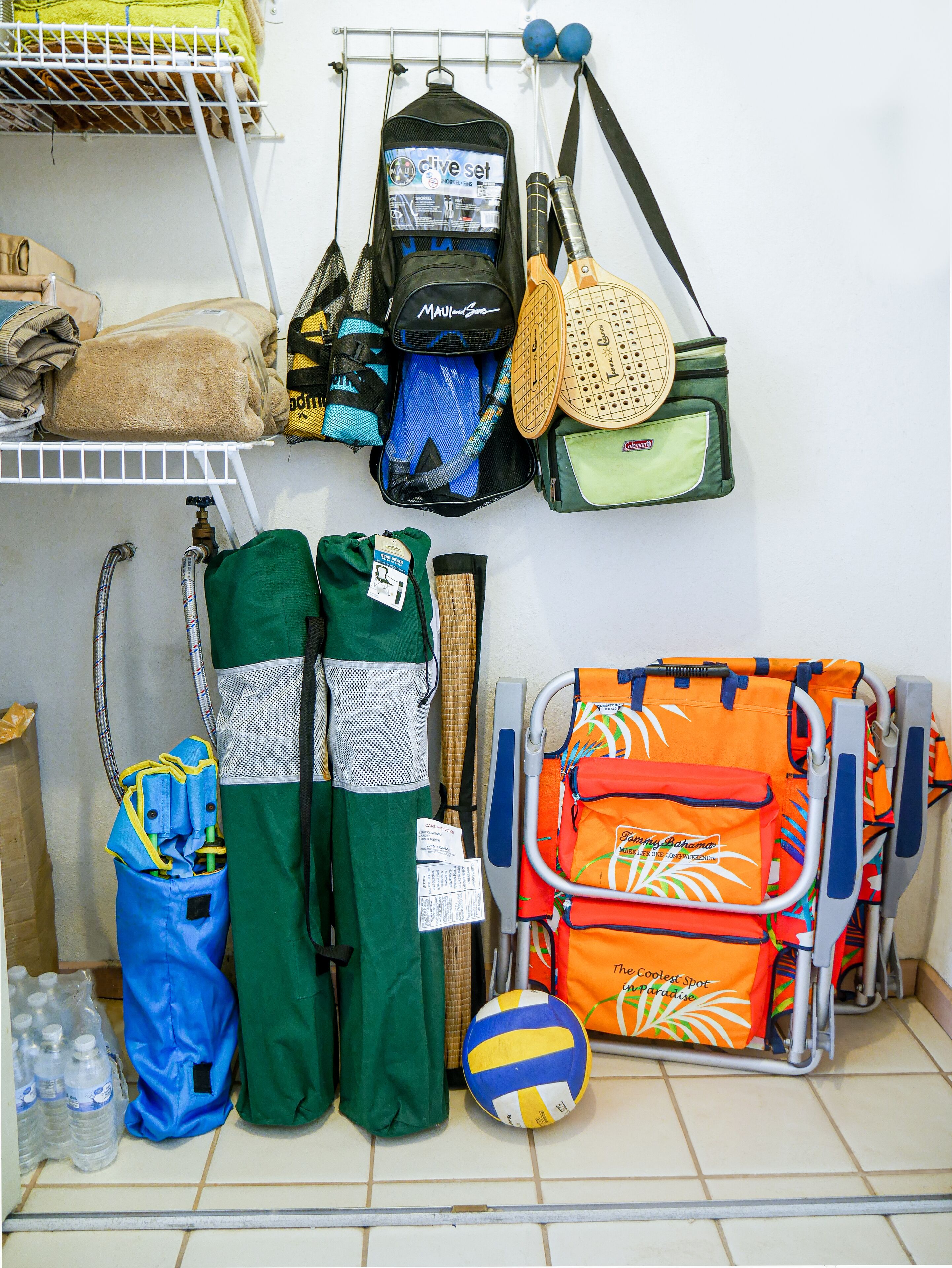 A storage area with various sports equipment, including a volleyball, a tennis racket, and bags.