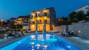 A poolside area with lounge chairs, a swimming pool, and a building with multiple balconies. - Apartments Sutalo (Konavle)