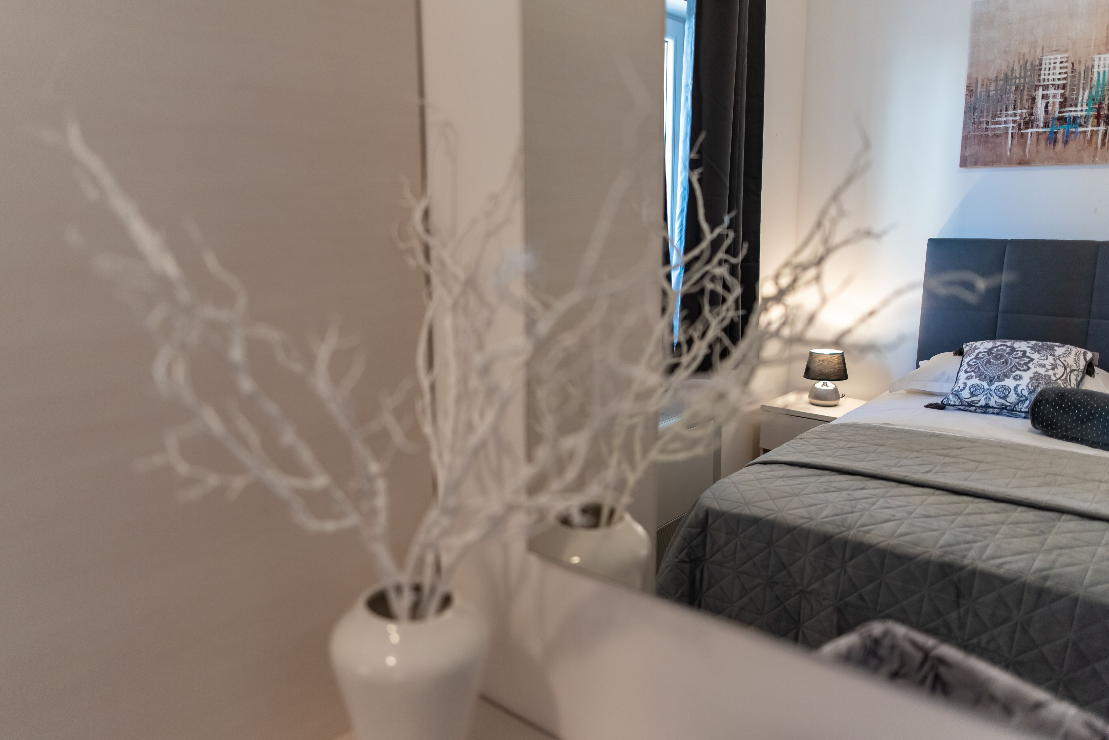 A bedroom with a bed, bedside table, lamp, and decorative branches in white vases.