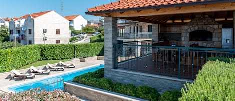 A pool with lounge chairs, a stone building with a tiled roof, and a stone fireplace.
