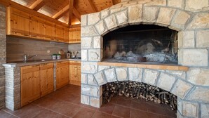 A kitchen with stone fireplace, wooden cabinets, and a tiled floor. - Apartments Sutalo (Konavle)