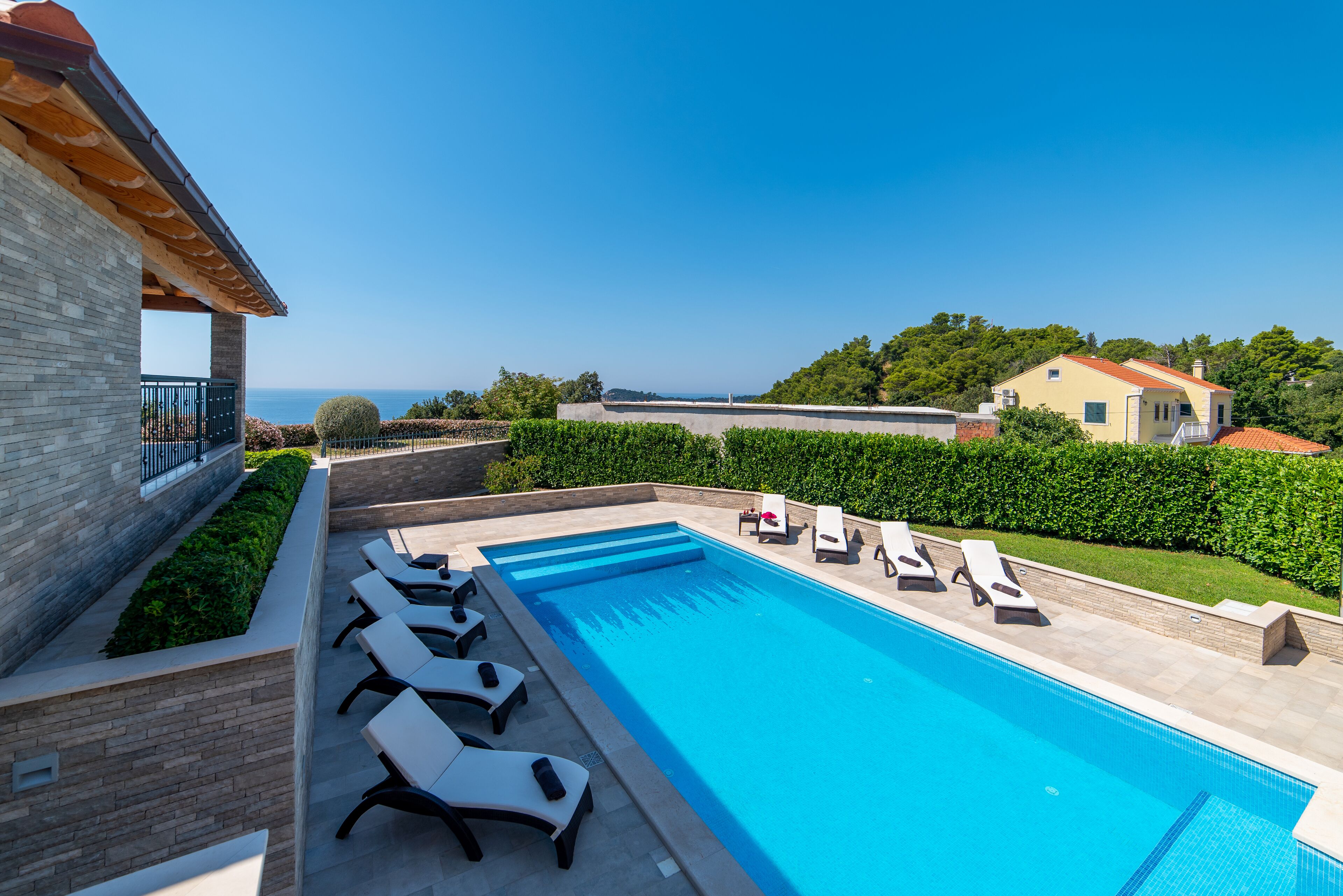 A swimming pool with lounge chairs, a view of the sea, and a building with a tiled roof.