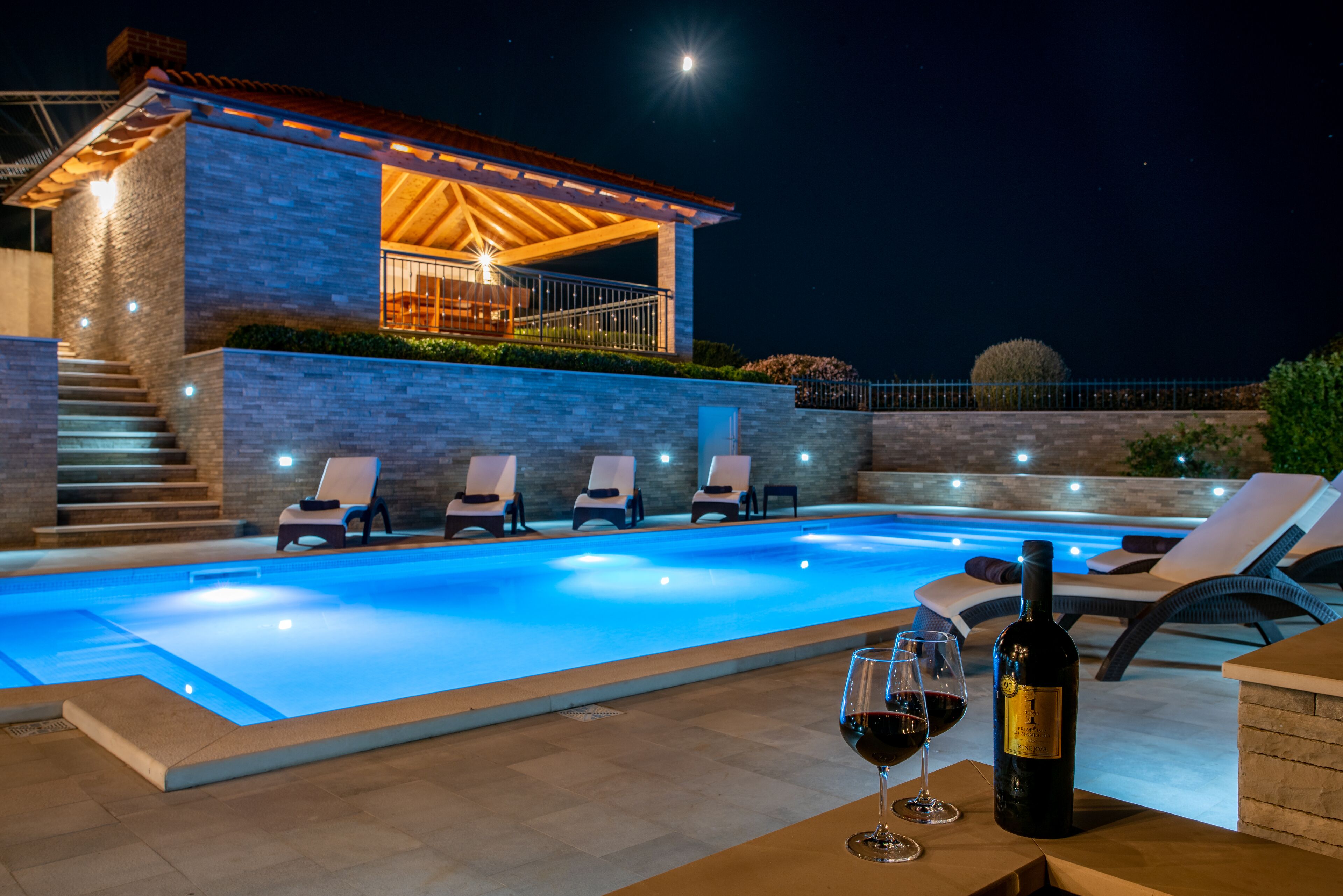 A swimming pool with lounge chairs and a bottle of wine.