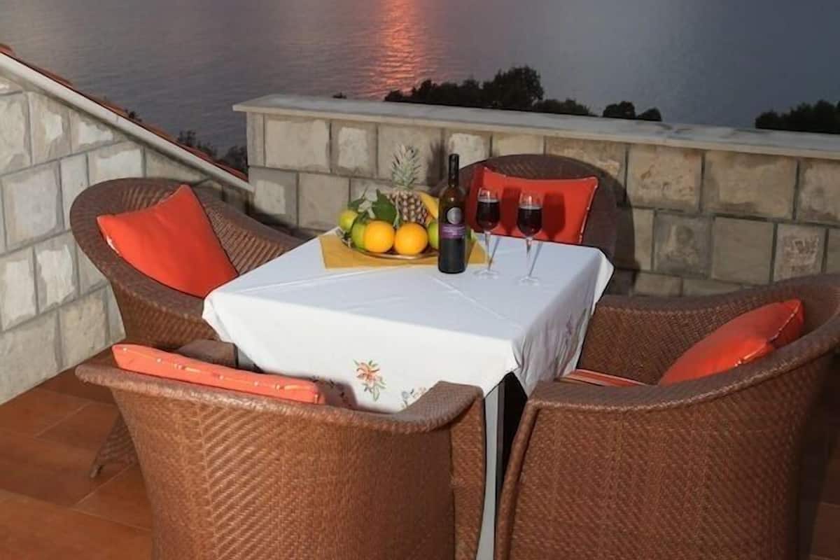 A dining area with wicker chairs and a table set for two, overlooking a sunset over the sea.
