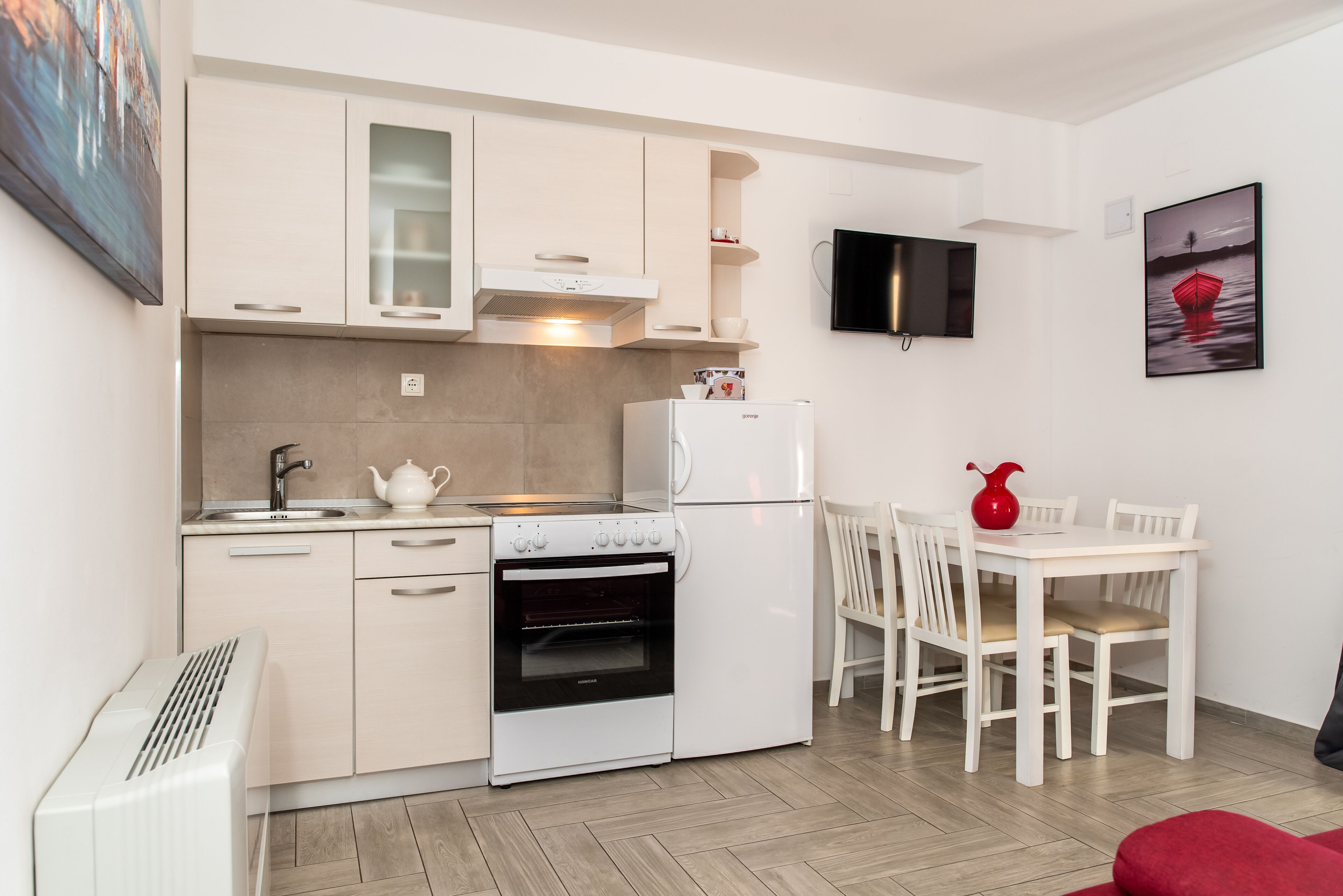 Cocina compacta con muebles blancos, horno integrado, microondas y comedor con mesa y sillas.