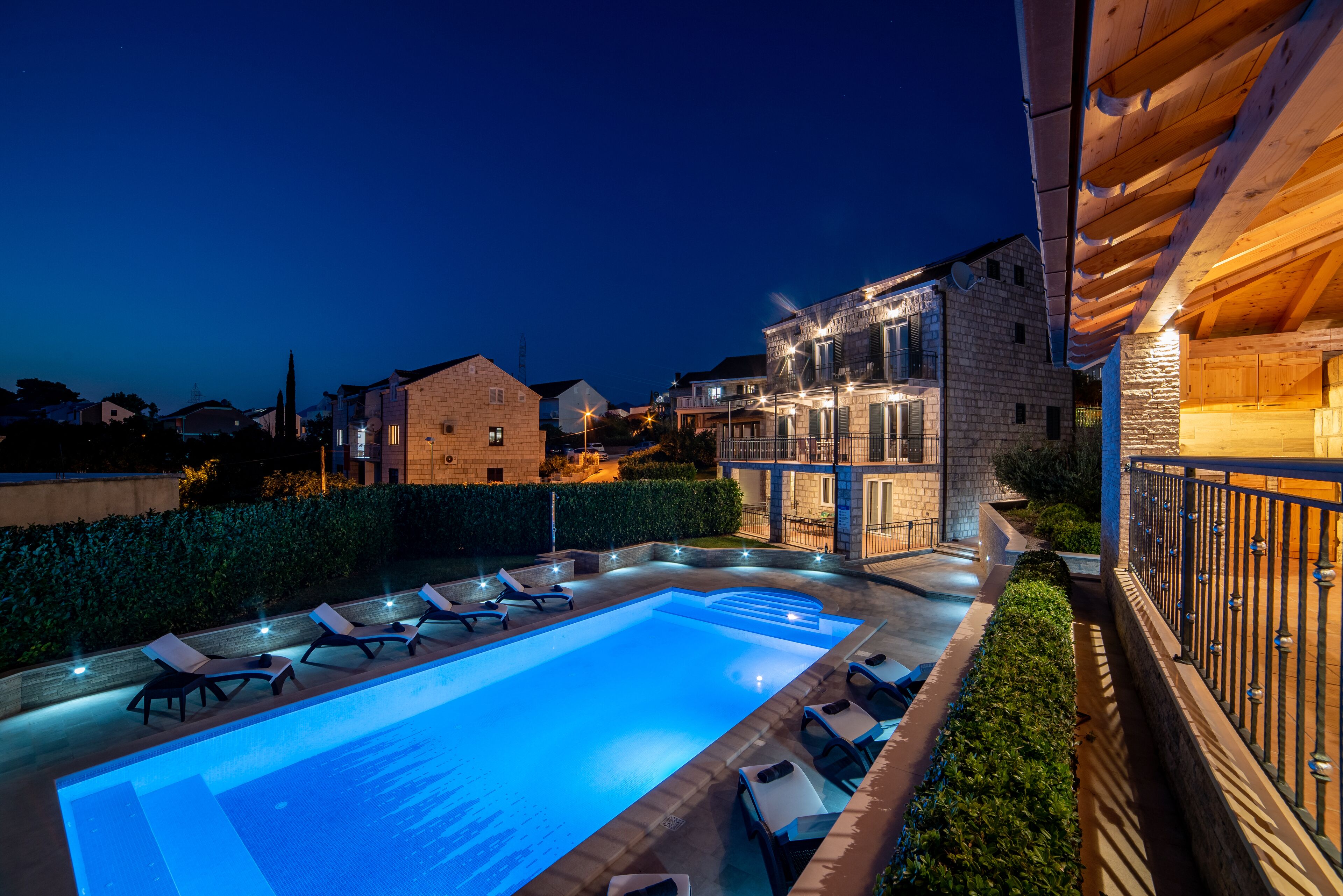 Une piscine avec des chaises longues, un bâtiment en pierre et une terrasse en bois dotée de rampes.