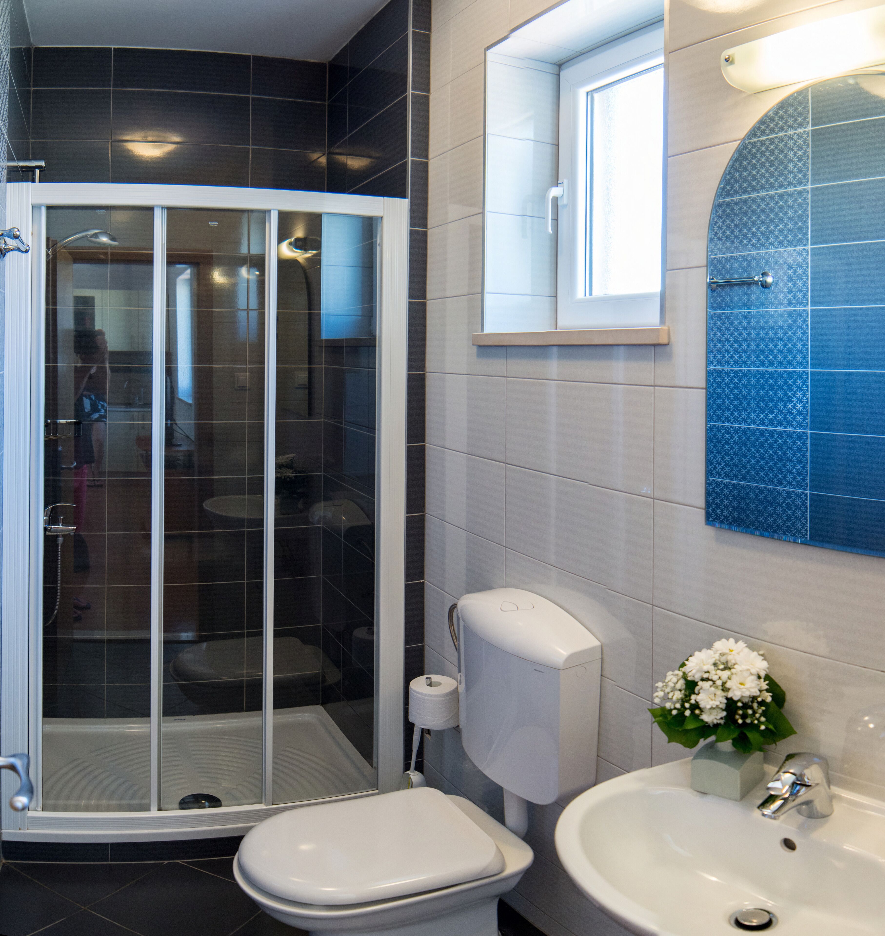 A modern bathroom with a shower enclosure, toilet, sink, and a small window.