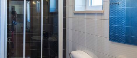 A modern bathroom with a shower enclosure, toilet, sink, and a small window.