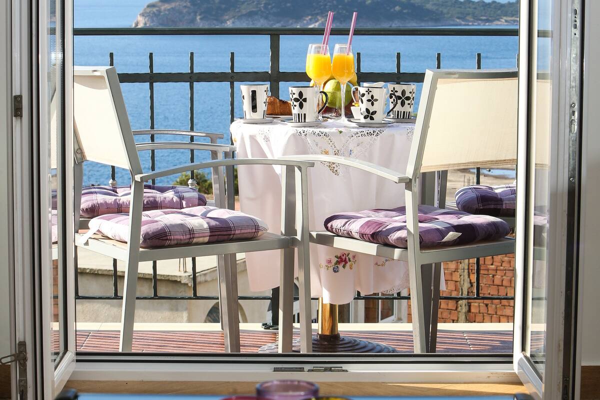 A balcony with a table set for two, overlooking a coastal view.
