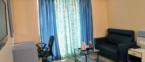 A compact living room with a desk, a black office chair, a dark blue sofa, and a small table with a glass top.