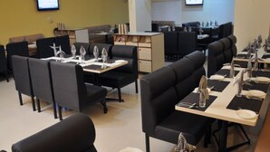 Ein Restaurant mit schwarzen Polsterbänken, weißen Tischgedecken und einer gelben Wand.