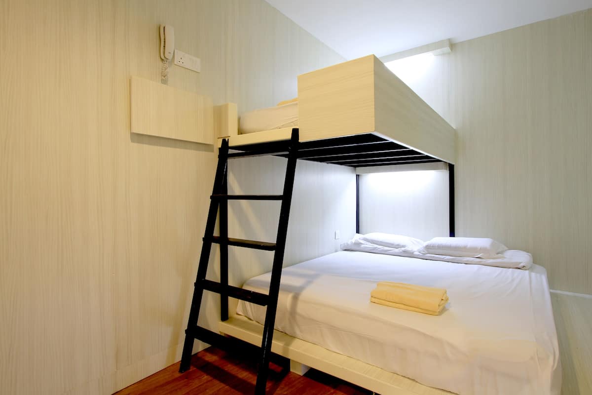 A bunk bed with a ladder, white bedding, and a small wooden shelf above the top bunk.